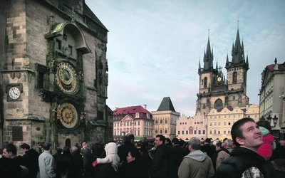 Prágai óváros tér emberekkel, háttérben az Orloj óramű és a Týn-templom látható.