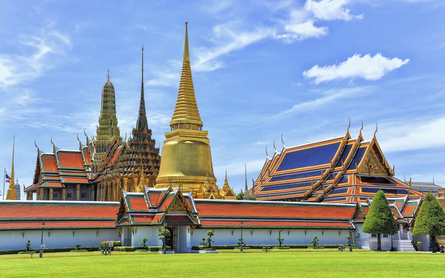 Királyi Palota Bangkokban – a templom sztúpái aranyozottak, a tetőket fénylő narancssárga és zöld cserepek borítják.