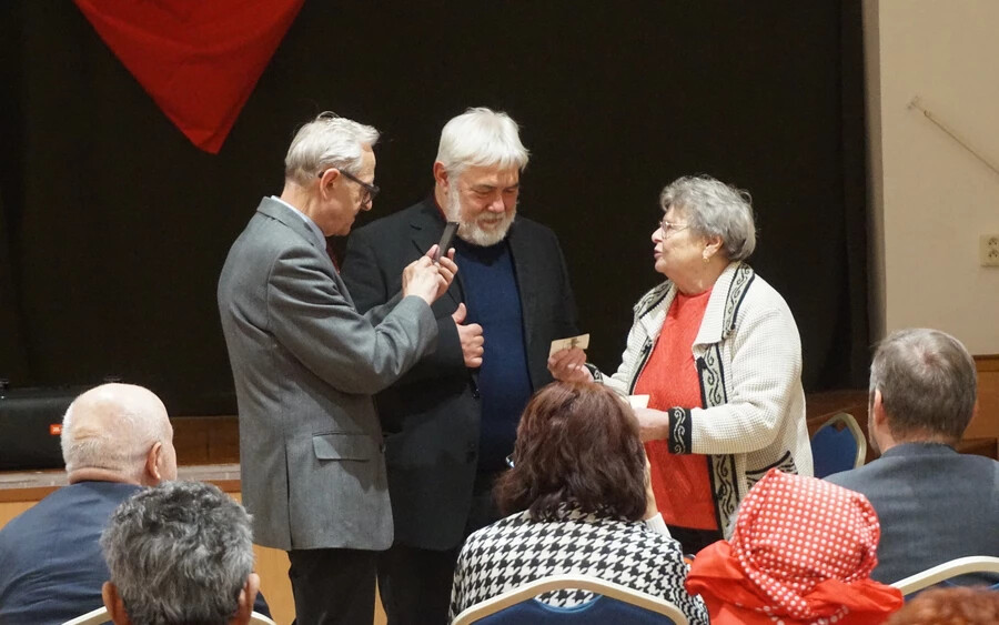 Neviďanský Mária Grzegorz Łubczyknak (baloldalon) és Molnár Imrének mutatja az édesapja képét, amelyen a lengyel asszonyok által kötött pulóvert hordja (a szerző felvétele)(Vataščin Péter felvétele)